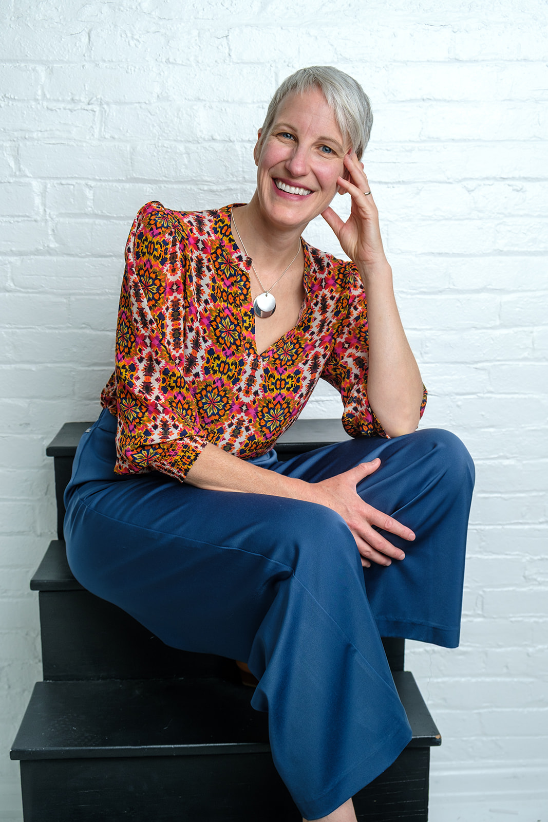 Kristen Peairs seated and smiling against a white brick wall